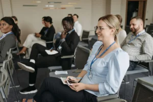 Woman smiles while seated with colleagues during a conference presentation